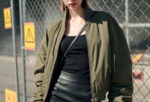 Young European woman in a yellow hard hat posing by a construction fence in harsh sunlight wearing a leather mini skirt and combat boots