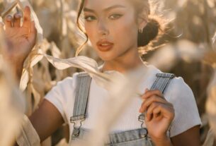 Stunning young woman peeking through tall corn stalks in a cornfield maze at golden hour, wearing denim overalls, photoreal 8K