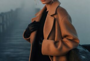 Stunning young woman on a foggy wooden pier wearing a long wool coat and leather gloves, cinematic dawn haze, photoreal 8K