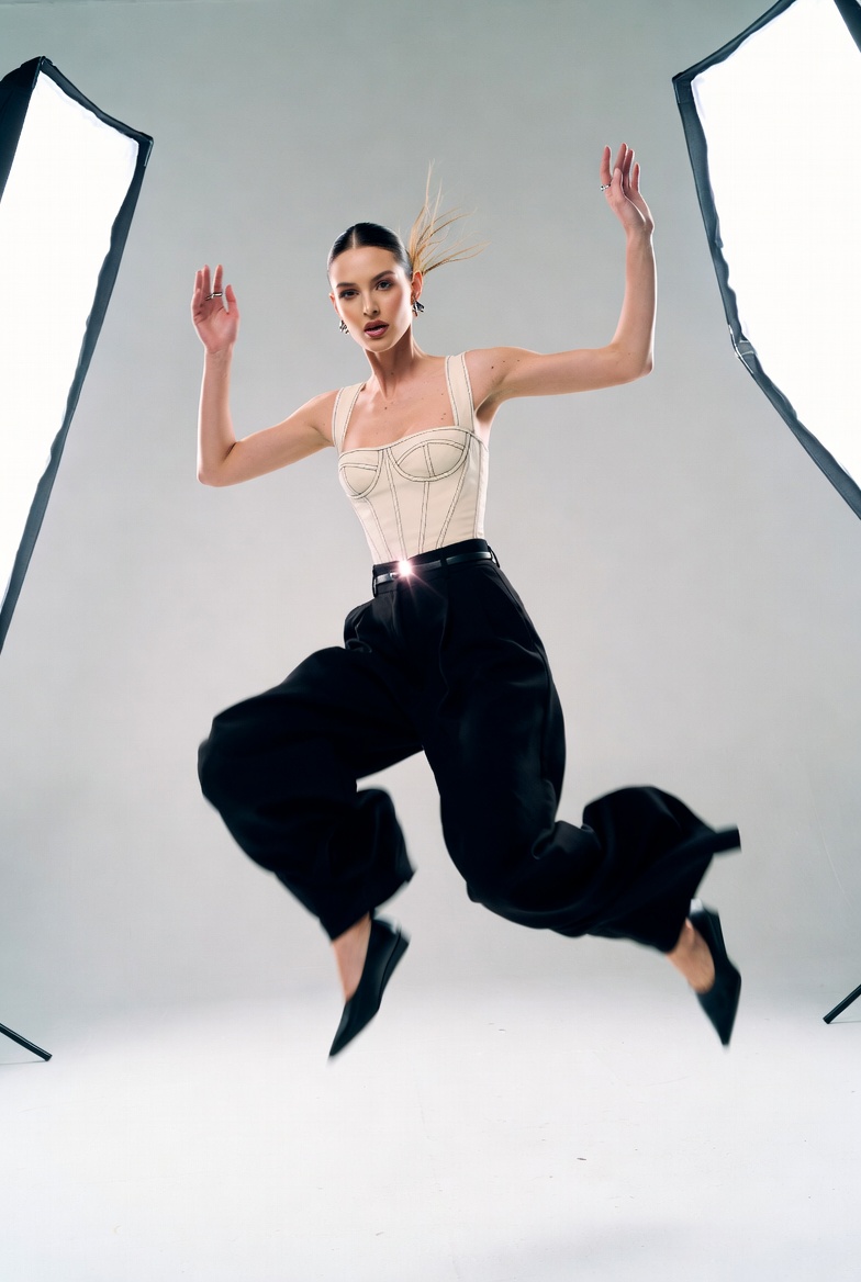 Stunning young woman mid-jump in a white cyclorama studio with high-key lighting, wearing a modern high-fashion outfit, photoreal 8K