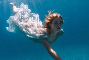 European woman swimming underwater in a flowing dress with sun rays and bubbles in a crystal blue pool