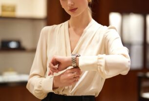 Young European woman trying on a luxury watch at a glass counter inside a high-end watch boutique with soft spotlights and blurred background
