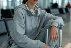 Stunning young woman sitting on a suitcase at an airport departure terminal wearing a grey tracksuit and designer sneakers, cinematic terminal lighting, photoreal 8K