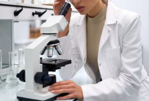 Stunning young woman in a modern science lab wearing a tailored lab coat and safety glasses, leaning toward a microscope under clean white light, photoreal 8K