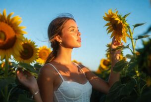 Stunning young woman in a tall sunflower field under a blue sky wearing a white corset top and light shorts, sunlit cinematic photoreal 8K look